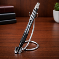 Metallic black pen with textured grip on a chrome pen stand, wooden desk background