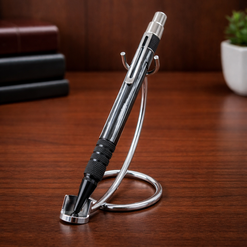 Metallic black pen with textured grip on a chrome pen stand, wooden desk background